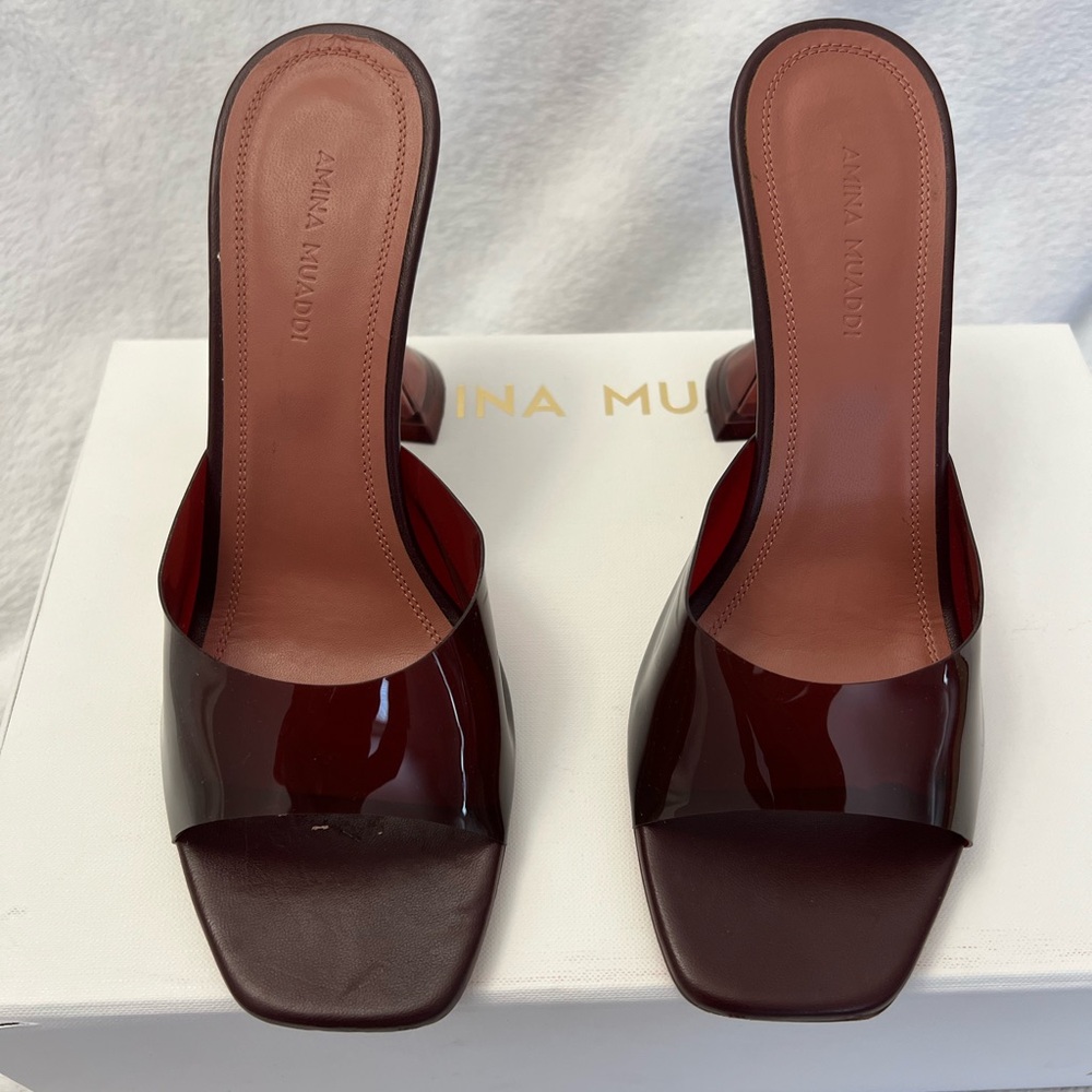 Authentic Amina Muaddi Lupita Glass mules in a rich wine / burgundy tone.